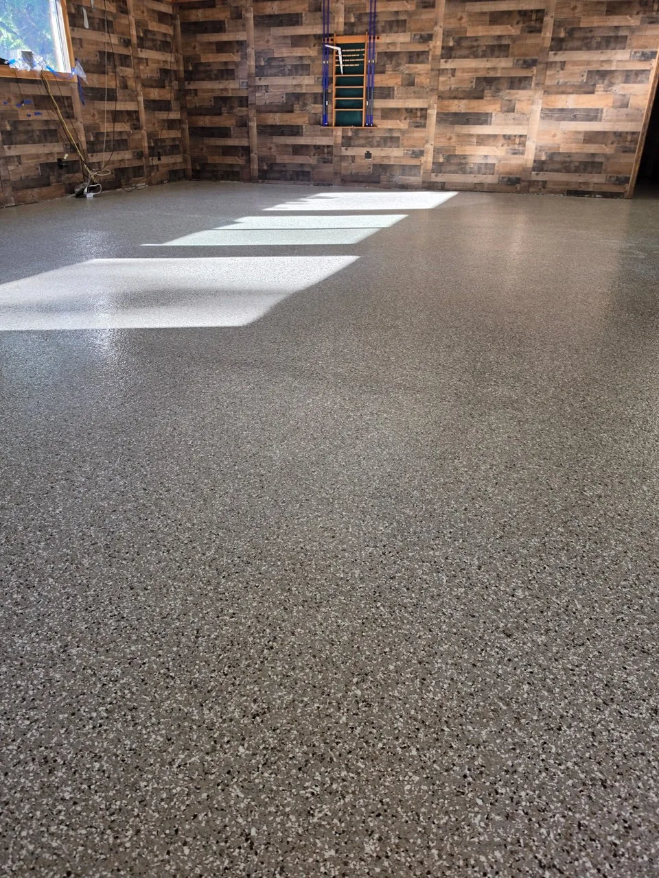 High-gloss full-flake epoxy floor in tan, beige, brown and white granite blend at Rocking Chair Resort game room with rustic wood walls