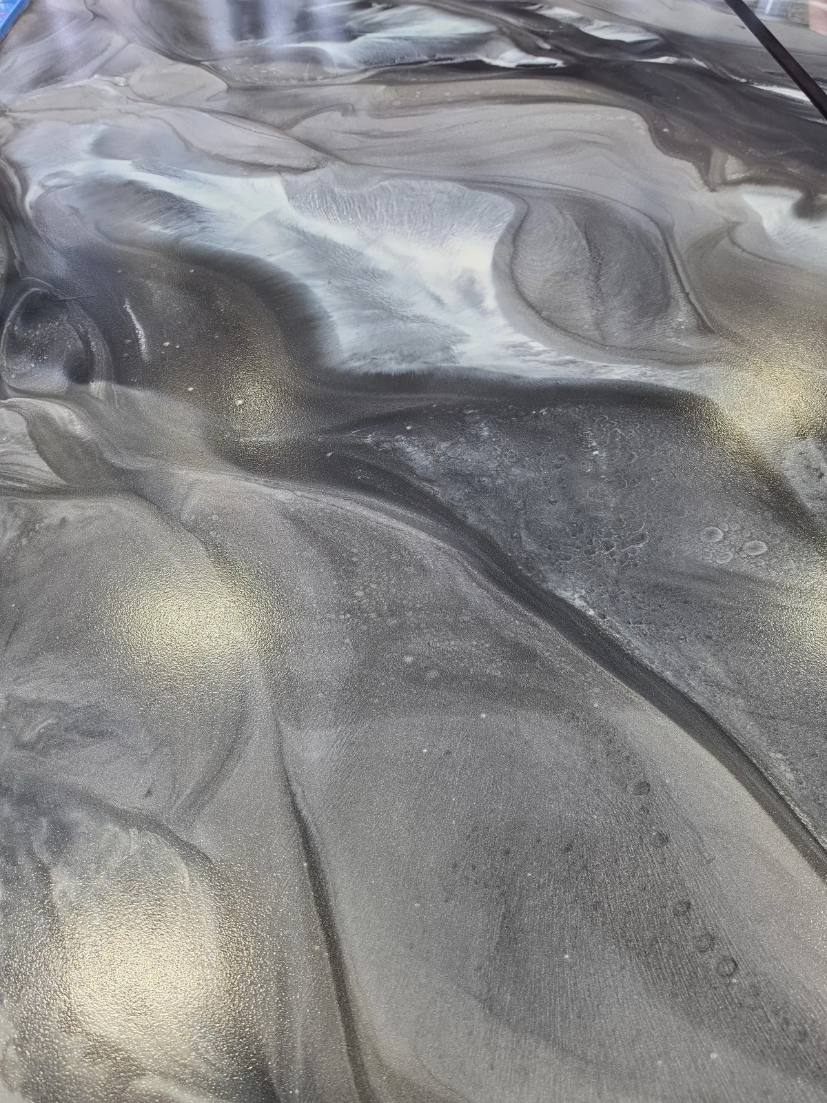 Close-up of a glossy metallic epoxy floor with flowing silver, charcoal and white marble-like swirls