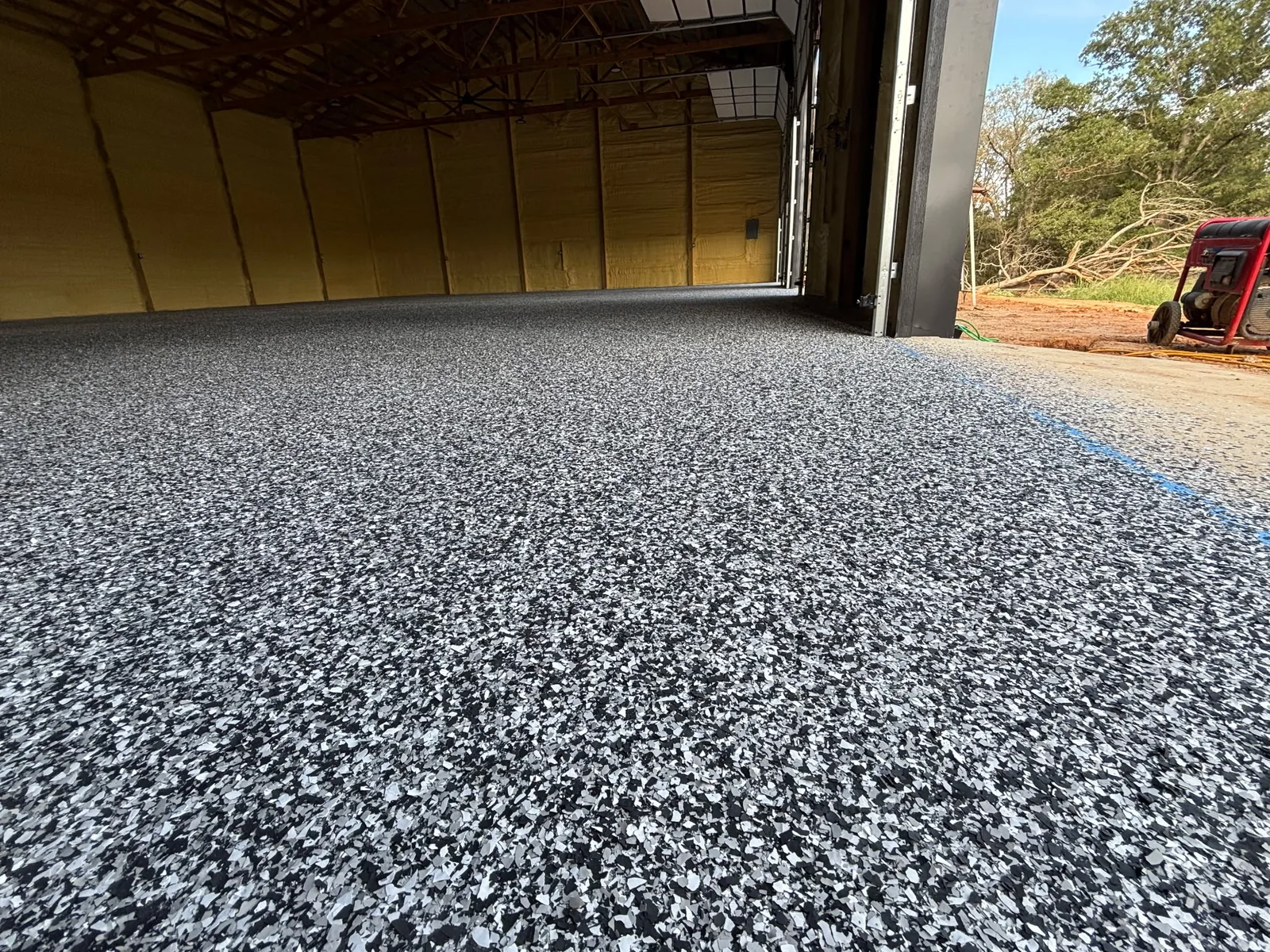 Wide view of a completed black, white and gray decorative flake epoxy floor across a large insulated shop