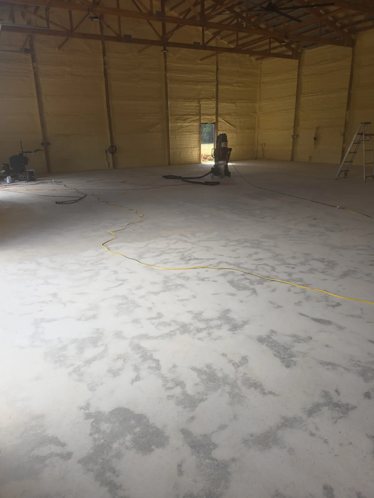 Large shop interior with ground bare concrete floor, spray-foam insulated walls and a floor grinder before the epoxy coating